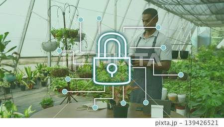 Using tablet greenhouse worker updating plants behind table with padlock overlay, copy space 139426521