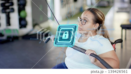 Gripping wheelchair user in blue tee and glasses at gym, pulling cable bar with holographic lock Gripping wheelchair user in blue tee and glasses at gym, pulling cable bar with holographic lock 139426561