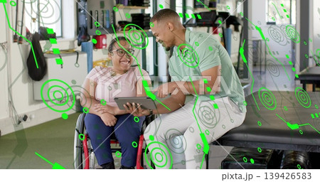 Adult woman in wheelchair wearing pink tee navy pants reviewing tablet with therapist in rehab gym 139426583