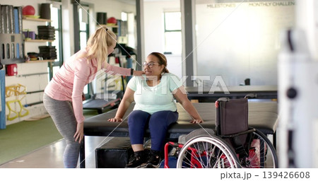 Guiding therapist leaning over patient in mint shirt on therapy table at clinic, wheelchair nearby 139426608