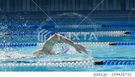 Female swimmer performing front crawl in racing pool, wearing swim cap and goggles with lane ropes Female swimmer performing front crawl in racing pool, wearing swim cap and goggles with lane ropes 139426712