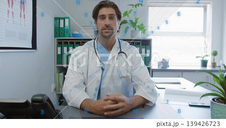 Mid adult doctor wearing coat reviewing paperwork, smartphone in consultation room with stethoscope 139426723