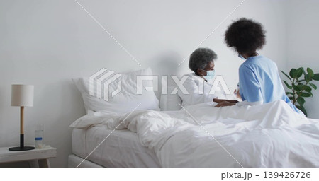 Leaning healthcare worker in scrubs holding gowned patient arm at bedside with lamp, copy space 139426726
