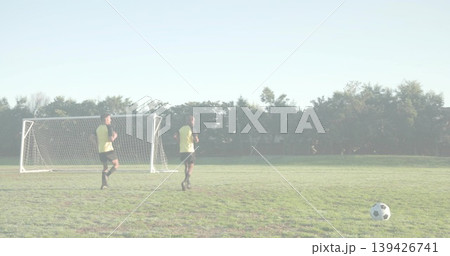 Jogging players wearing training vests, black shorts on park field, with portable goal, soccer ball 139426741