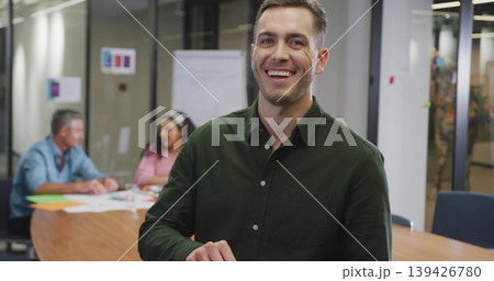 Smiling man wearing dark green shirt standing by wooden table in meeting room, reviewing papers Smiling man wearing dark green shirt standing by wooden table in meeting room, reviewing papers 139426780