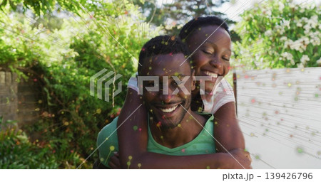 Smiling man carrying partner piggyback in lush backyard garden, with colored dots and lines overlay 139426796