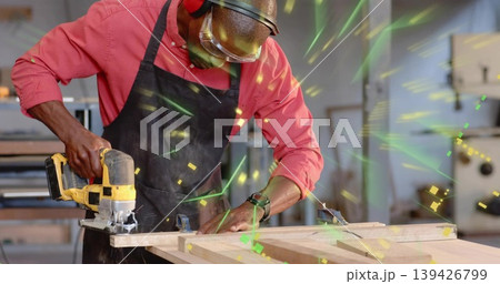 Cutting wooden plank with handheld jigsaw saw in woodworking shop, wearing apron and safety goggles Cutting wooden plank with handheld jigsaw saw in woodworking shop, wearing apron and safety goggles 139426799