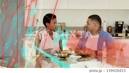Chatting couple eating burgers in modern kitchen, glass dining table with sauce and beverage bottle Chatting couple eating burgers in modern kitchen, glass dining table with sauce and beverage bottle 139426815