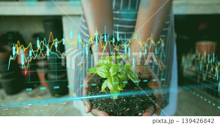 Gardener holding seedling in soil at greenhouse bench with striped apron and digital graph overlay 139426842
