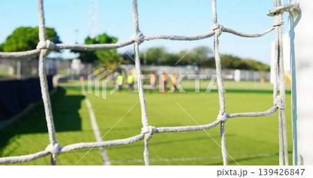 Framing white knotted goal net and right goalpost at club soccer pitch, players wearing bright bibs 139426847