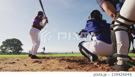 Batting, maroon batter swinging in batter's box at baseball field, catcher in blue gear, copy space 139426848