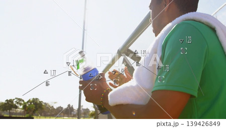 Sitting athlete in green shirt with towel holding bottle on bleachers beside field, HUD, copy space 139426849