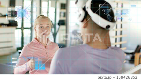 Holding small weight, woman in pink top coaching partner with VR headset at gym, AR graphics Holding small weight, woman in pink top coaching partner with VR headset at gym, AR graphics 139426852