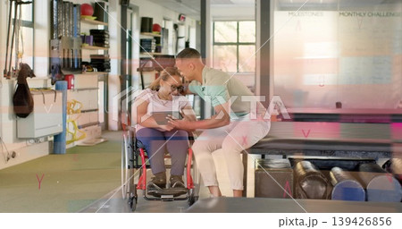 Leaning, man in light green polo and woman in wheelchair reviewing tablet near whiteboard in rehab Leaning, man in light green polo and woman in wheelchair reviewing tablet near whiteboard in rehab 139426856