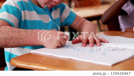 Writing student in turquoise tee leaning on spiral notebook in classroom, solving math with pencil Writing student in turquoise tee leaning on spiral notebook in classroom, solving math with pencil 139426947