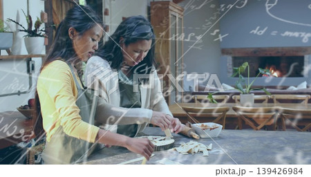 Preparing two women making lattice tart at wooden counter in home kitchen, with rolling pin, aprons 139426984