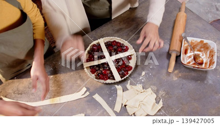 Assembling pair placing pastry lattice over cherry tart on home kitchen counter, wearing yellow top Assembling pair placing pastry lattice over cherry tart on home kitchen counter, wearing yellow top 139427005