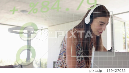 Leaning woman wearing patterned top and white headset typing on laptop in home office HUD overlays Leaning woman wearing patterned top and white headset typing on laptop in home office HUD overlays 139427083