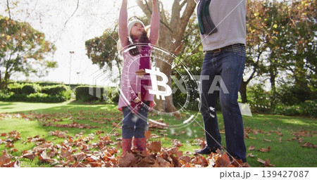 Tossing leaves dad wearing scarf, daughter in pink coat knit hat boots park with Bitcoin hologram 139427087