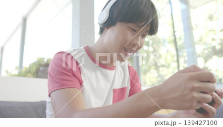Playing on handheld device, adult male wearing pink raglan T-shirt and headphones in living room Playing on handheld device, adult male wearing pink raglan T-shirt and headphones in living room 139427100