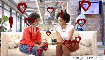 Chatting pair wearing red blouse and white top holding coffee, device on office sofa, red hearts Chatting pair wearing red blouse and white top holding coffee, device on office sofa, red hearts 139427168