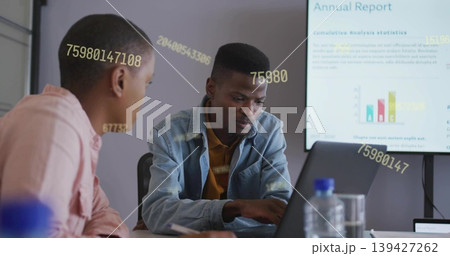 Working male at conference table typing on laptop in denim jacket, with yellow overlays on display 139427262