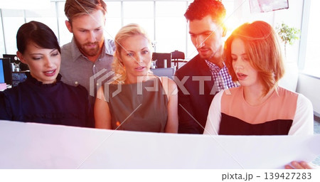Reviewing five colleagues leaning over poster in bright office, wearing professional attire Reviewing five colleagues leaning over poster in bright office, wearing professional attire 139427283