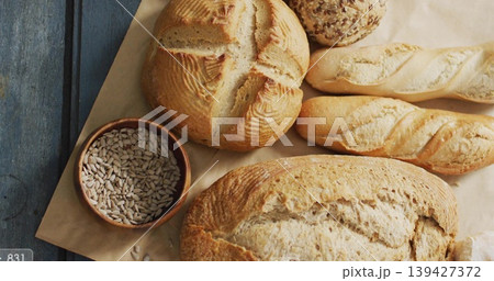 Displaying round boule, baguette, seeded roll on painted blue table with wooden bowl of seeds 139427372