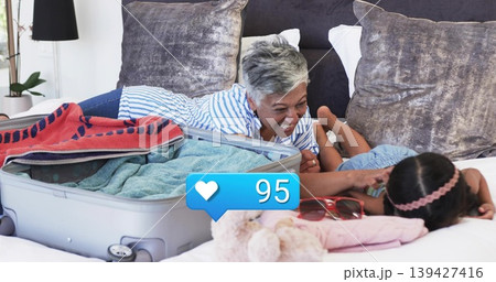 Laughing woman in striped top reaching toward child with pink headband on bed, suitcase, heart 95 Laughing woman in striped top reaching toward child with pink headband on bed, suitcase, heart 95 139427416