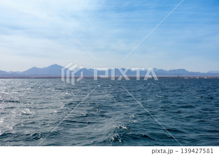 Serene ocean waves and distant mountain landscape under clear blue sky Serene ocean waves and distant mountain landscape under clear blue sky 139427581