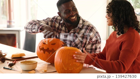 Carving couple wearing plaid shirt and rust sweater working at home table, with pumpkins and tools Carving couple wearing plaid shirt and rust sweater working at home table, with pumpkins and tools 139427630