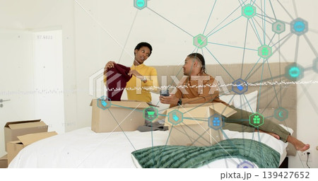 Holding burgundy sweater, couple wearing yellow top brown top showing phone in bedroom with boxes 139427652