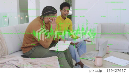 Reviewing papers, two adults wearing yellow top on sofa at home, with laptop and green waveform Reviewing papers, two adults wearing yellow top on sofa at home, with laptop and green waveform 139427657