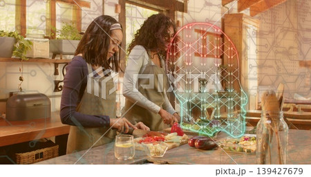Chopping two women wearing olive aprons preparing vegetables on wooden kitchen island, neon overlay Chopping two women wearing olive aprons preparing vegetables on wooden kitchen island, neon overlay 139427679