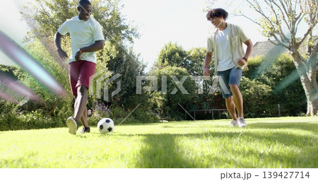 Kicking two adult men wearing casual summer clothes and sneakers on backyard lawn, with soccer ball Kicking two adult men wearing casual summer clothes and sneakers on backyard lawn, with soccer ball 139427714