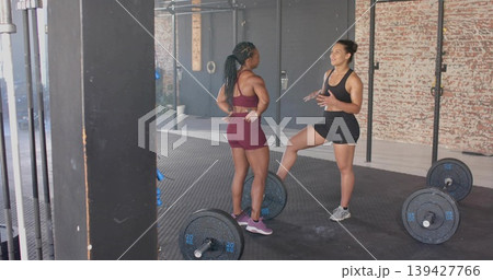Coaching trainer and trainee women wearing maroon and black sportswear in gym, with loaded barbells Coaching trainer and trainee women wearing maroon and black sportswear in gym, with loaded barbells 139427766