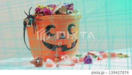 Showing orange jack o'lantern bucket holding wrapped candy on white desk, spider, turquoise grid Showing orange jack o'lantern bucket holding wrapped candy on white desk, spider, turquoise grid 139427874