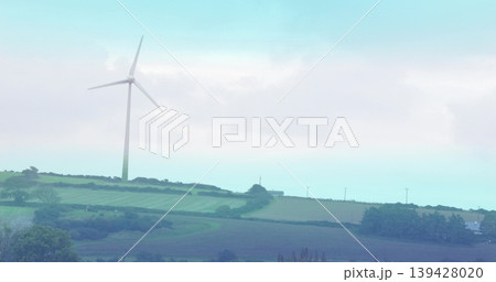 Spinning white wind turbine sweeping blades on low ridge over farm fields, hedgerows, utility poles Spinning white wind turbine sweeping blades on low ridge over farm fields, hedgerows, utility poles 139428020