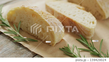 Displaying sliced rustic bread resting on weathered wooden table, with parchment, rosemary, crumbs 139428024