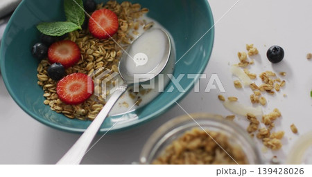 Showing teal bowl on white table with milk granola berries spoon scattered crumbs blurred jar Showing teal bowl on white table with milk granola berries spoon scattered crumbs blurred jar 139428026