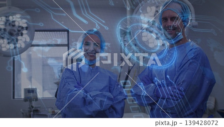 Standing surgeons in blue gowns and masks crossing arms smiling in operating room with digital HUD 139428072