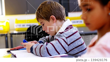 Leaning boy writing in class in gray maroon-striped top holding blue pen and notebook, math overlay 139428176
