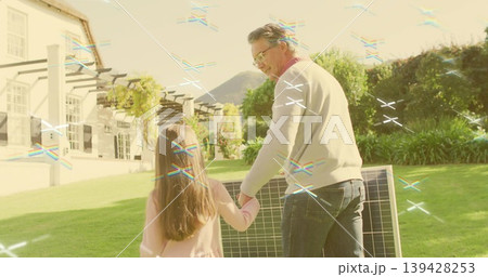 Walking dad in light sweater, jeans, holding girl in pink top across yard, solar panel Walking dad in light sweater, jeans, holding girl in pink top across yard, solar panel 139428253