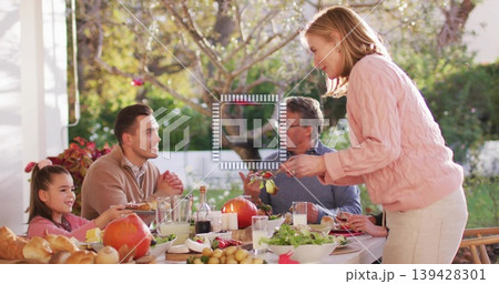 Serving pink-sweatered woman passing dish on covered porch with dining table, man in brown sweater Serving pink-sweatered woman passing dish on covered porch with dining table, man in brown sweater 139428301