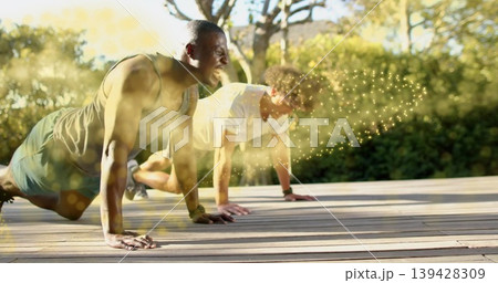 Doing push-ups two men wearing sports tops on wooden deck, with wristbands and golden flare 139428309