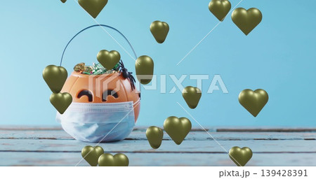 Showing orange pumpkin bucket wearing blue mask on painted table, with candies, spider, gold hearts 139428391