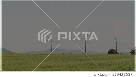 Standing three white wind turbines dominating midground of rural field, with low hills Standing three white wind turbines dominating midground of rural field, with low hills 139428557