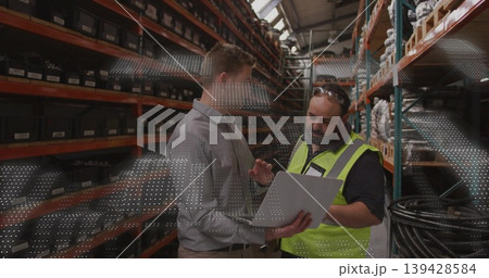 Holding tablet, two men wearing dress shirt and safety vest inspecting labeled bins in warehouse 139428584