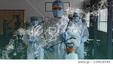 Disinfecting lead worker in full PPE operating handheld sprayer in gym, digital overlay Disinfecting lead worker in full PPE operating handheld sprayer in gym, digital overlay 139428599