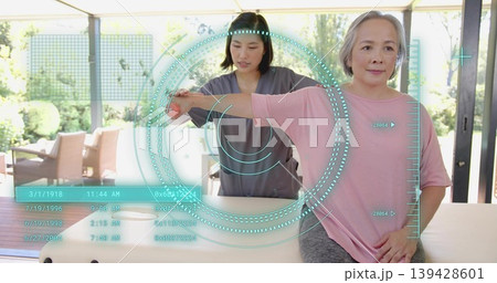 Assisting therapist in scrubs guiding client extending arm on padded table at home with AR HUD Assisting therapist in scrubs guiding client extending arm on padded table at home with AR HUD 139428601